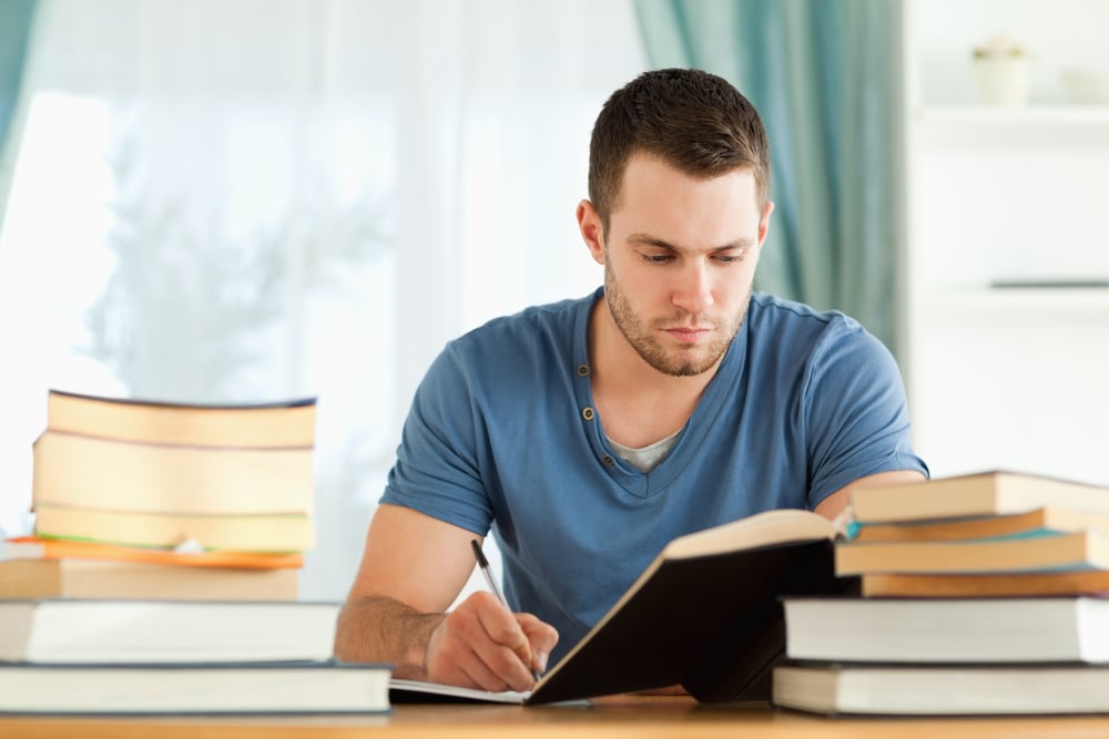 A man studying, surrounded by books.